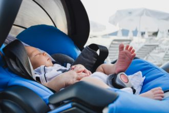 A newborn child in a car seat on the beach