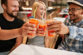 Happy diverse friends smiling while clinking glasses of orange juice