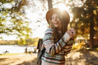 Stylish woman enjoying autumn weather in the sunny park. Enjoying nature. Fashion, style concept.