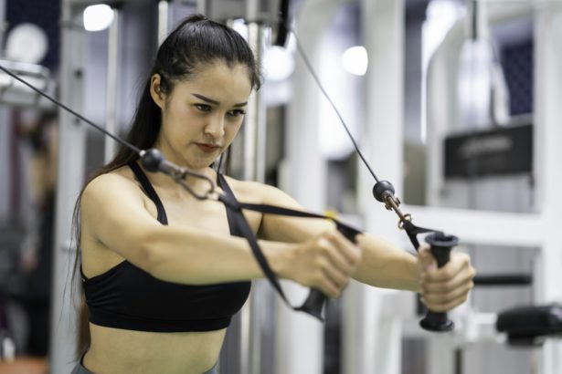 Young Asia lady exercise doing exercise-machine Cable Crossover fat burning workout in fitness class
