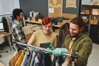 Young female volunteer with tablet making list of second hand clothes